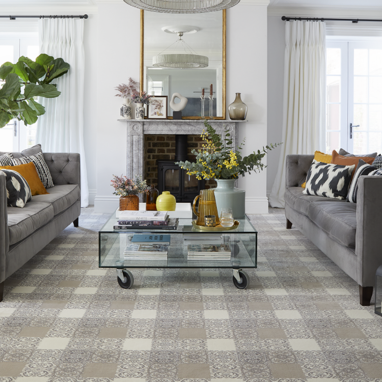 Two grey sofas and a glass coffee table on a square patterned grey and beige carpet