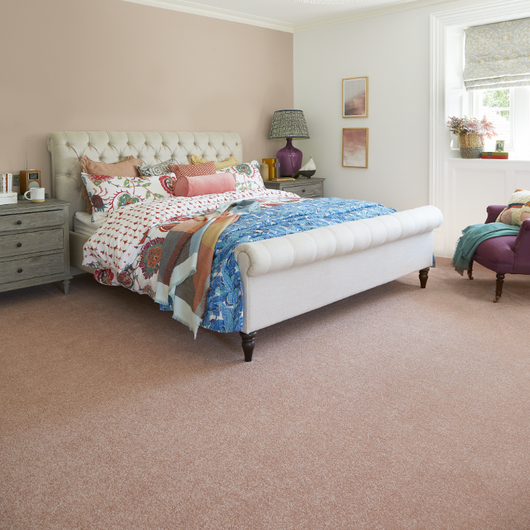 A pink bedroom with colourful bedspreads, white headboard and pink carpet