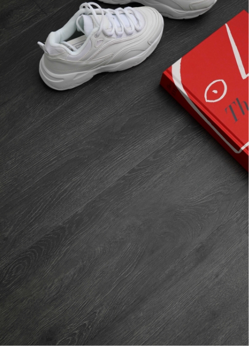 A close up shot of white trainers and a red book placed on a dark grey wood effect floor