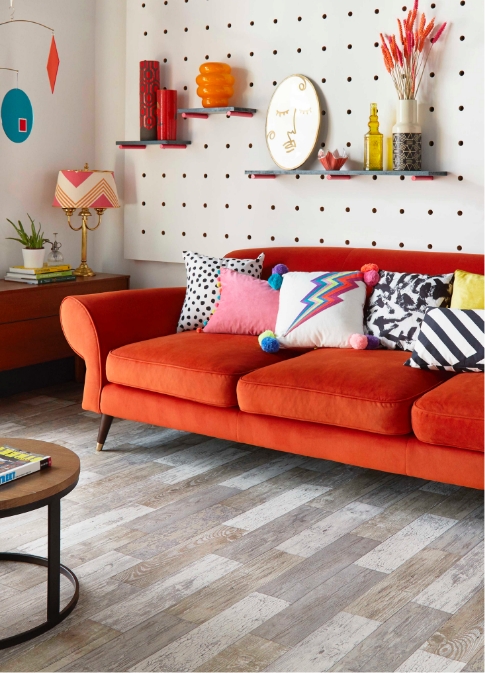 An orange sofa with bright coloured cushions is in front of a peg board, with stained plank flooring